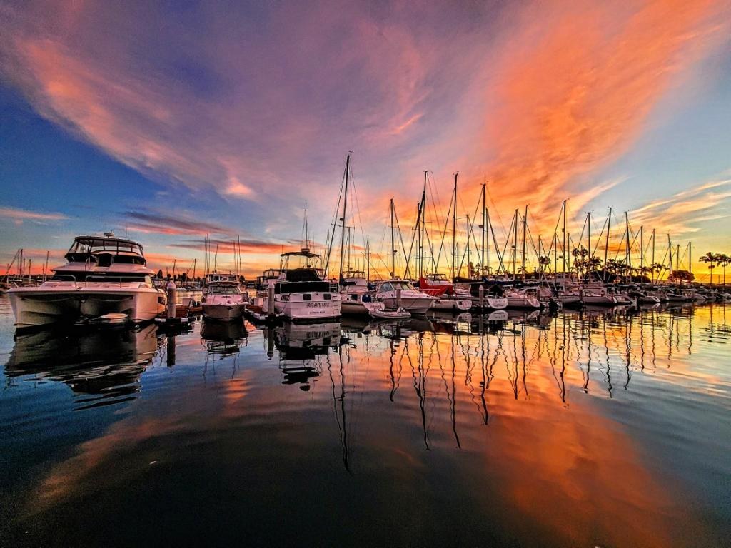 Shelter Cove Marina yachts and sailboats reflected in the water at a vivid San Diego sunset